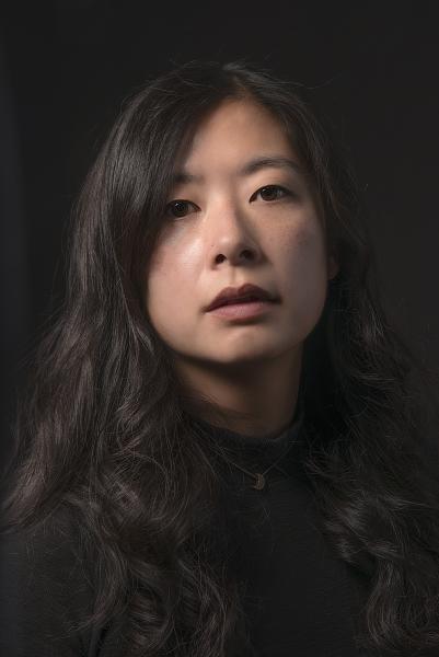 Portrait of Alyssa Songsiridej looking into the camera framed by her dark hair and a dark blouse