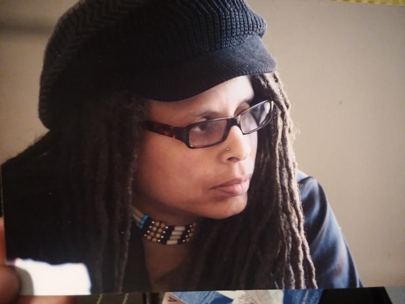 Photo of Jourdan Imani Keith looking off to the side wearing a black hat and black glasses
