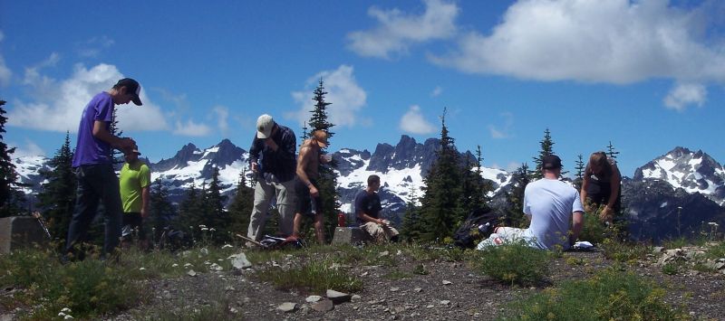Students standing on a mountain summit with jagged snow covered peaks in the background
