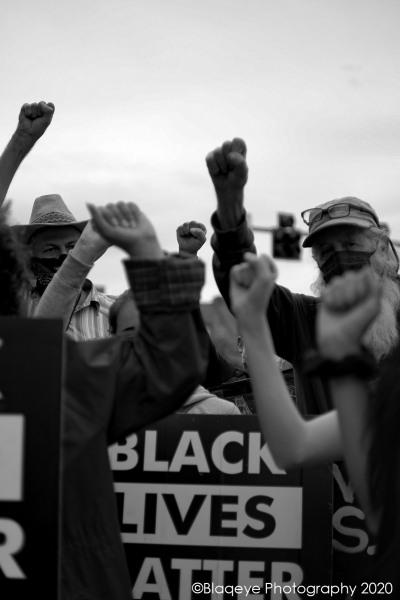 Demonstrators with fists raised and a black lives matter sign in center. Photo by Rasaan Burke.