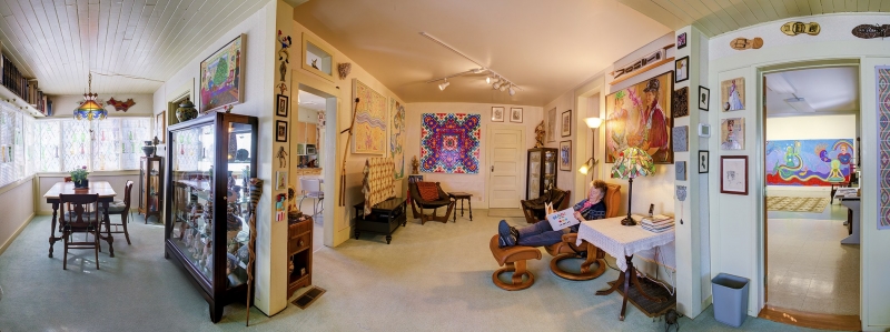 Wide angle photo of the interior of a home featuring colorful art and a reclining woman reading a book at center.