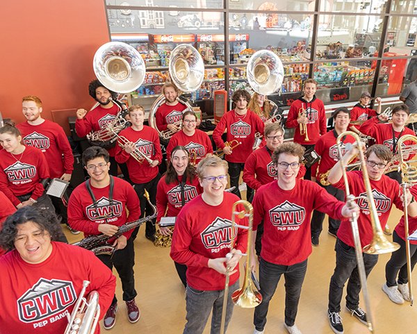 CWU Pep band smiling in matching crimson tees. They each hold their instrument out for the photo.