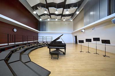 Photo of the CWU choral room. Risers on the left with a piano in the middle of the room.