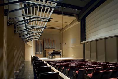 Photo of the recital hall stage from the back of the hall. The 9 foot Steinway D grand piano is center stage.