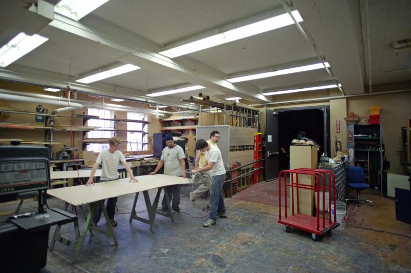 scene shop area. There are three men cutting a large piece of wood.