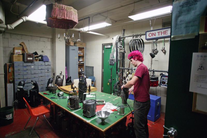 cwu theatre CTE room. There is a man with pink hair working at a green workshop desk.