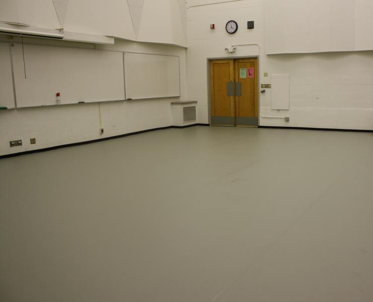 A dance studio room. There is a white board. The walls are built with brick and the doors are wooden.