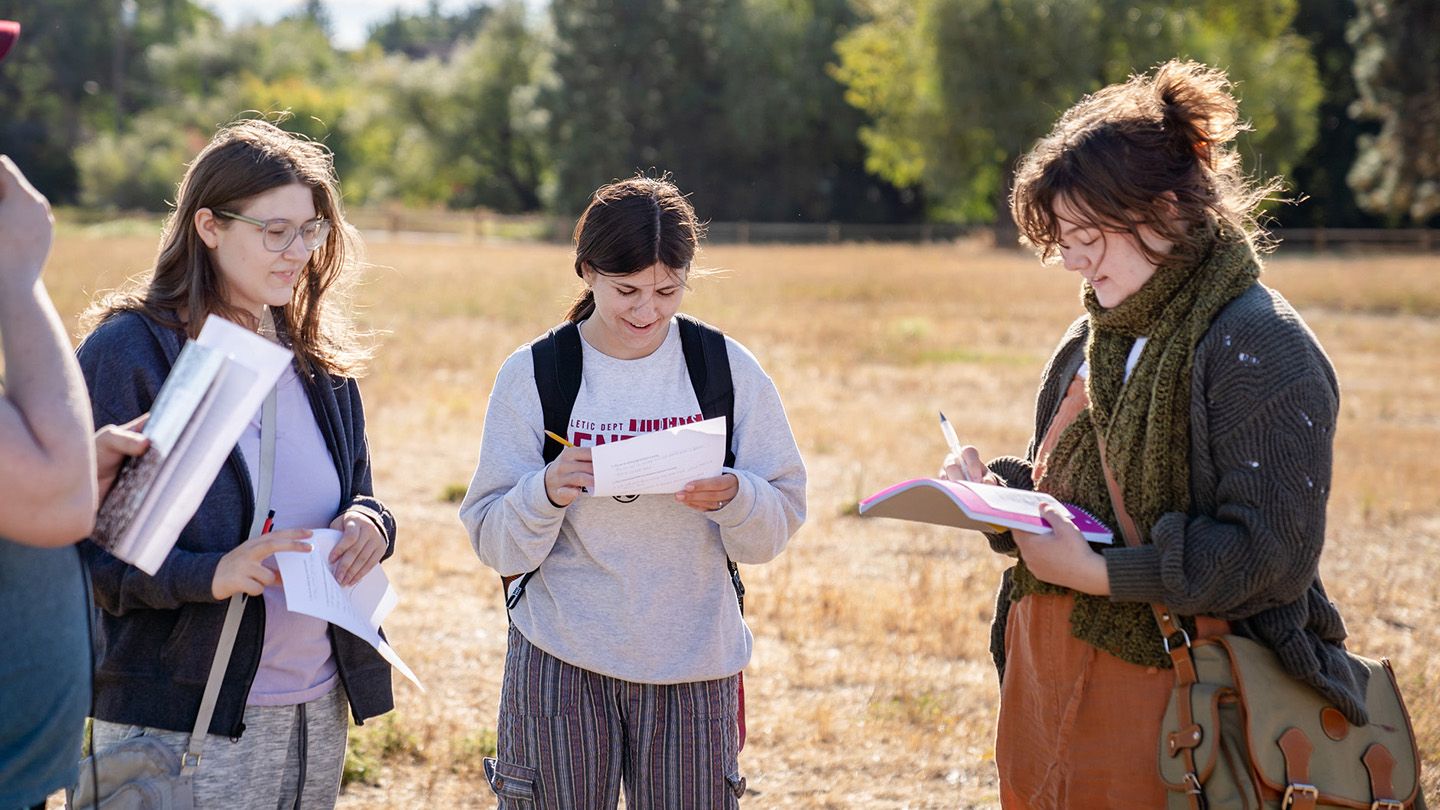 Three students at Central Washington University taking notes in a field.