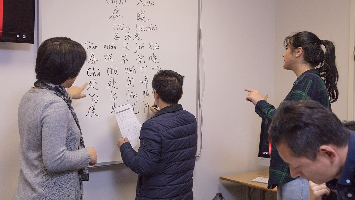 A professor within the asian studies department at Central Washington University takes the time to teach three students a new language and gives a visual representation on the white board.
