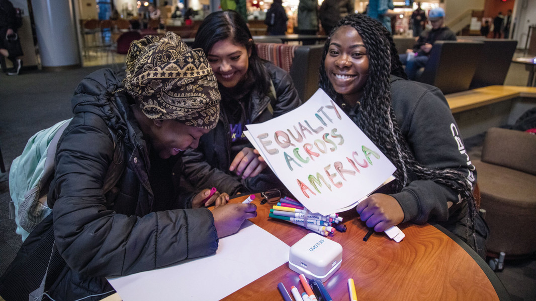 Three students at Central Washington University smile as they design a beautiful sign that reads "Equality Across America"