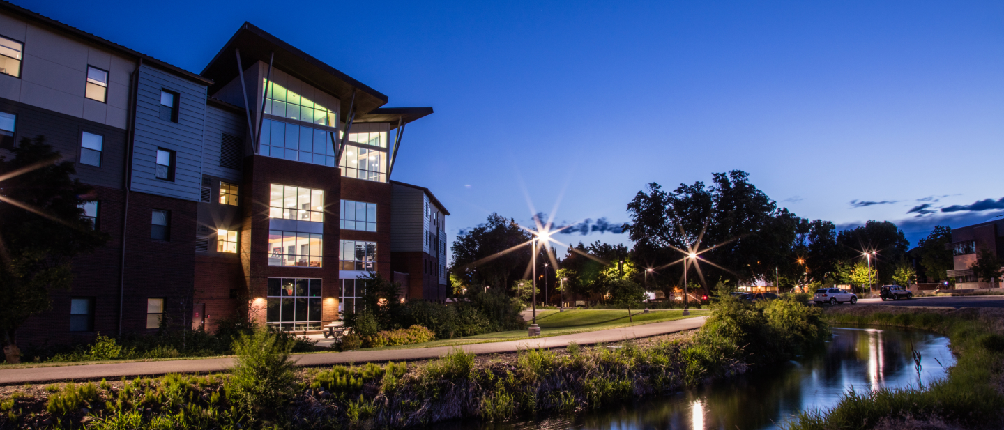 Northside of Barto Hall during dusk, lights in building are on, campus stream in the foreground