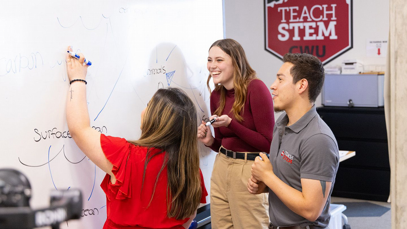 three students within the teach stem program at Central Washington University share a laugh as they write on the white board and learn something new.