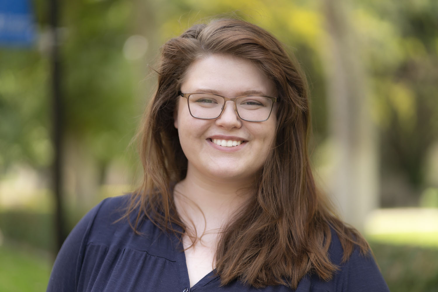 Person with brown hair past their shoulders, smiling with glasses.