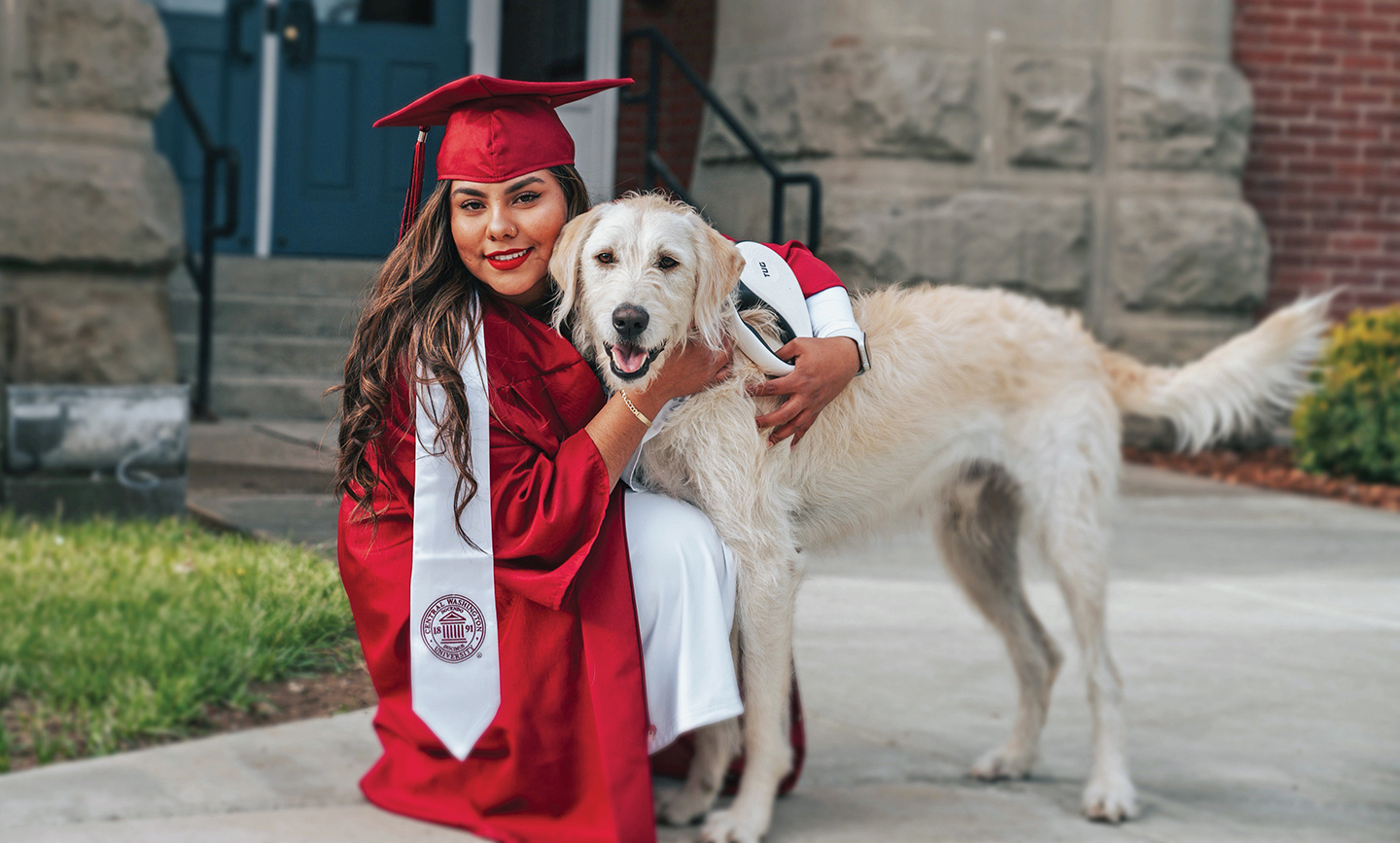 Angela Gonzalez in a CWU cap and gown, petting her dog