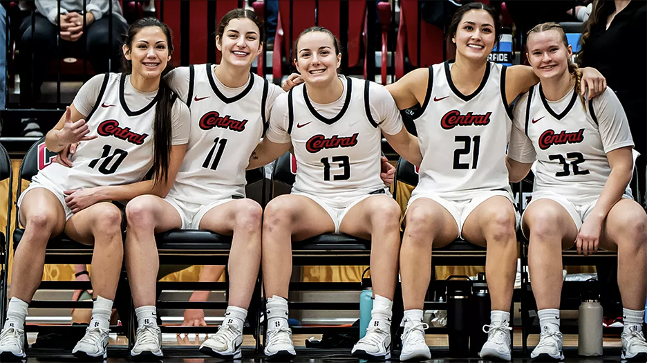 Five CWU players smile while sitting on the bench