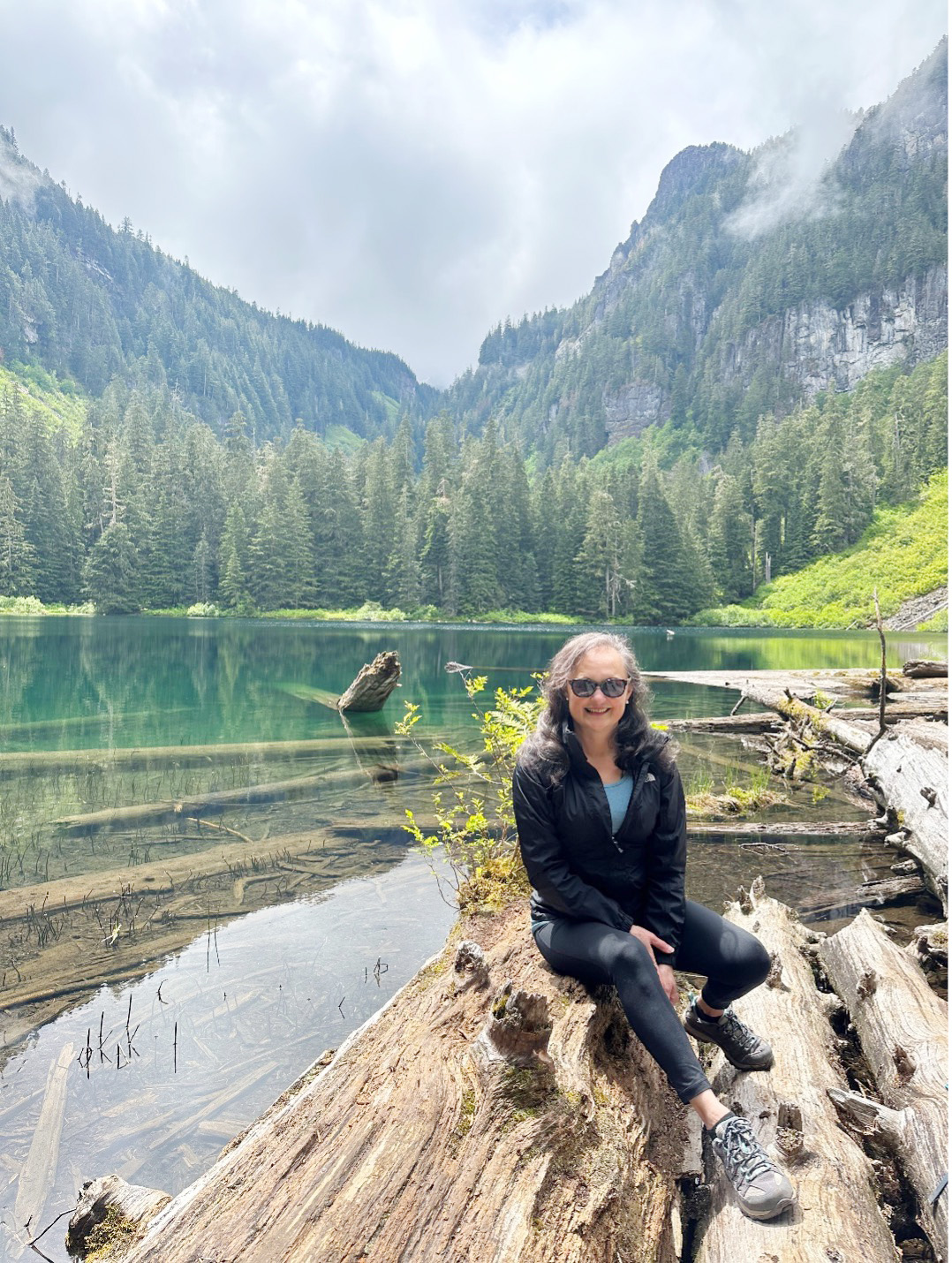 Conchita Chinchilla sits on a log with a lake behind her