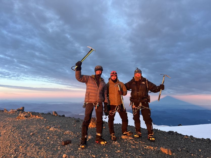 Three officers stand at the summit in the light of a sunrise.