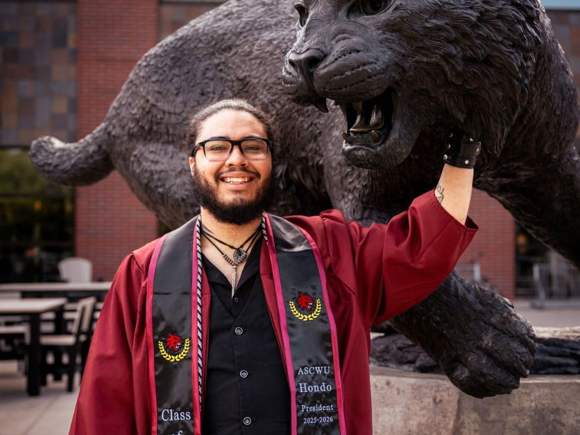 Hondo Acosta-Vega poses with the Wildcat statue in his graduation regalia
