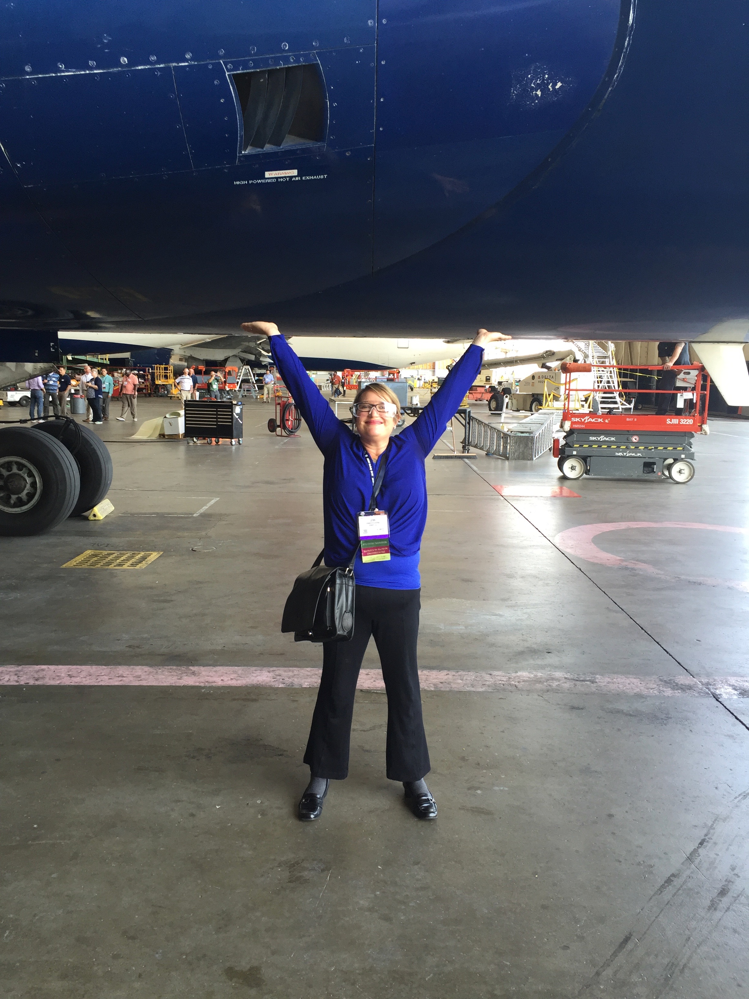 Jennifer Serne pretending to hold up an airplane that fills the top half of the frame