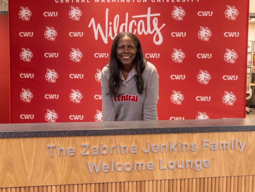 Zabrina Jenkins poses with the sign for the Zabrina Jenkins Family Welcome Lounge