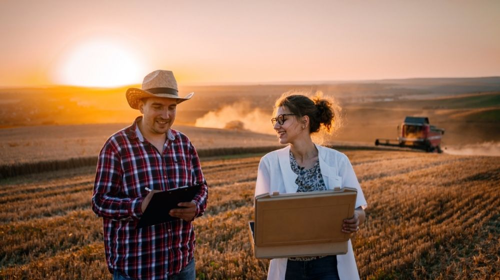 Male and female standing in a wheat field holding computers