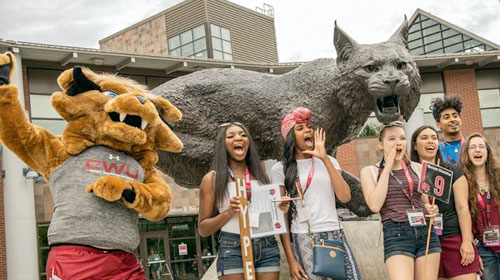 CWU students cheering in front of wildcat statute with CWU mascot.