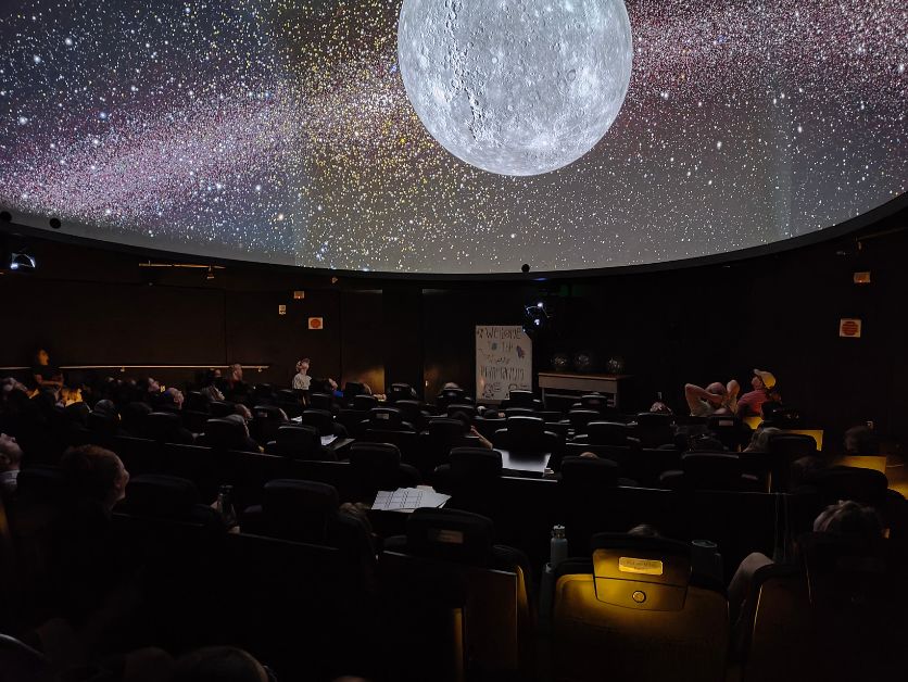 A crowd in the planetarium behold the moon's rise over a synthetic horizon