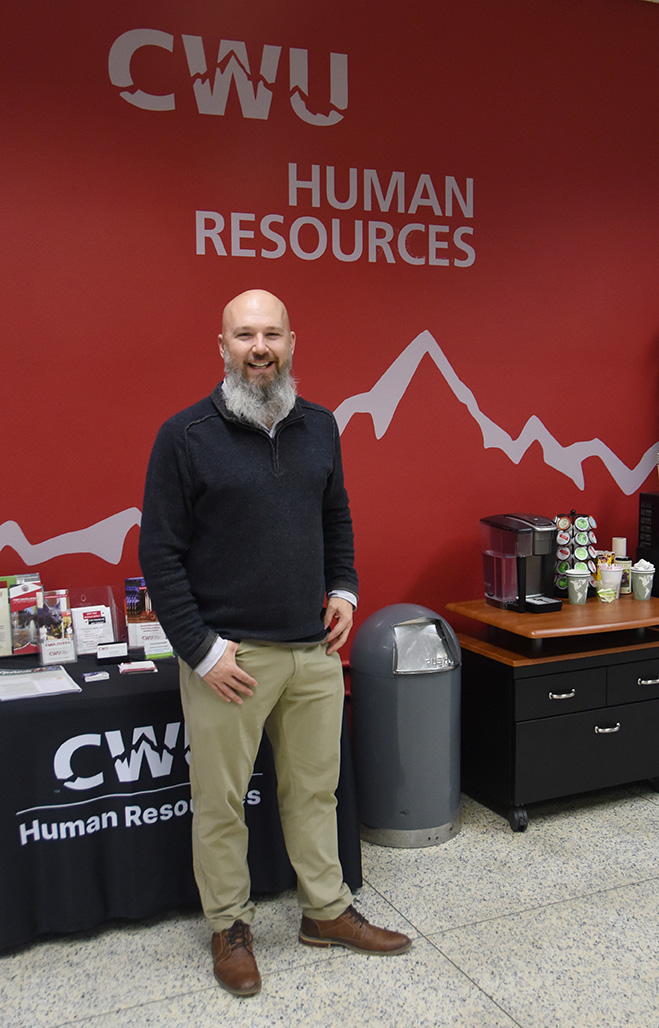 Joey Bryant stands in front of the Human Resources wall in Mitchell Hall.