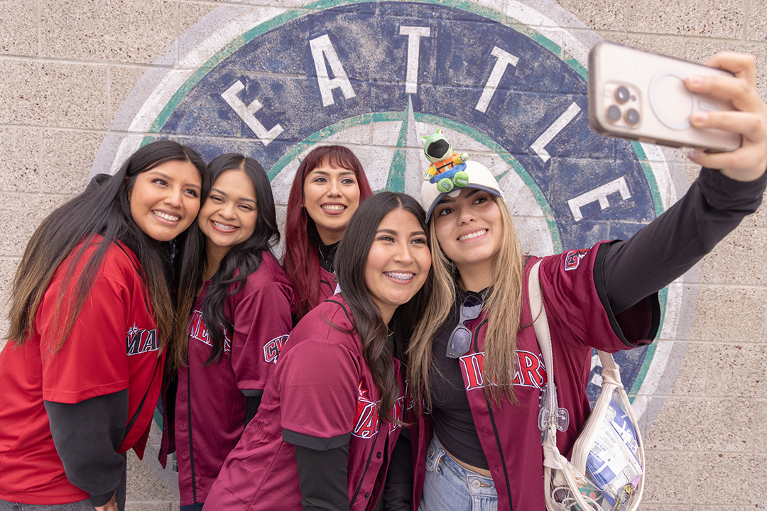 A group of five CWU alumnae snap a photo in front of the Seattle Mariners logo