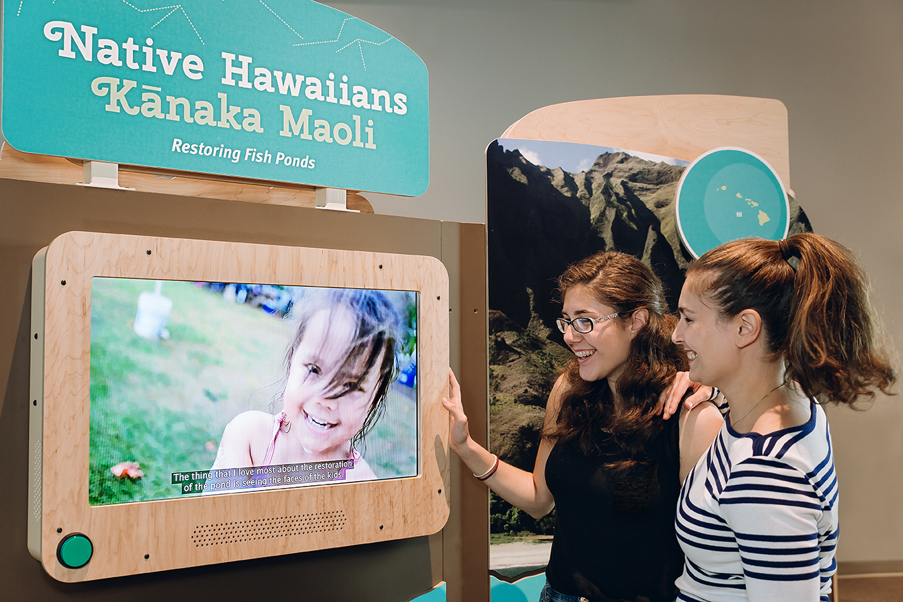 Two women look at a video display for Roots of Wisdom