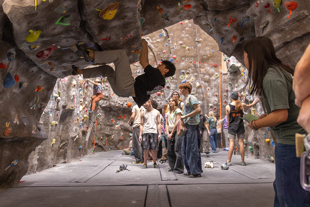A climber hanges upside down on the CWU climbing wall