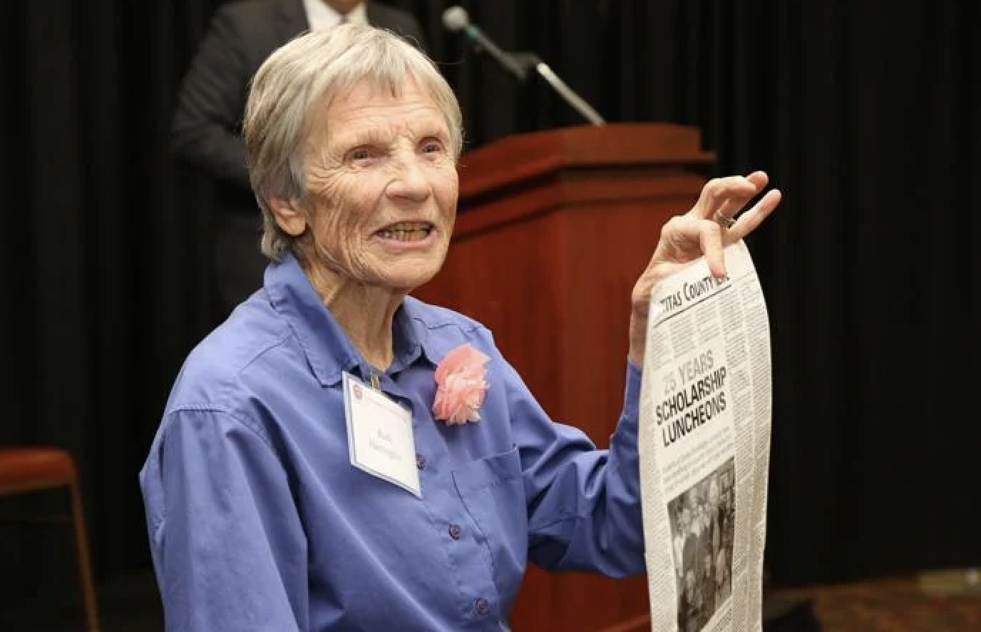 Ruth holds up a newspaper with a headline about the Scholarship Luncheons