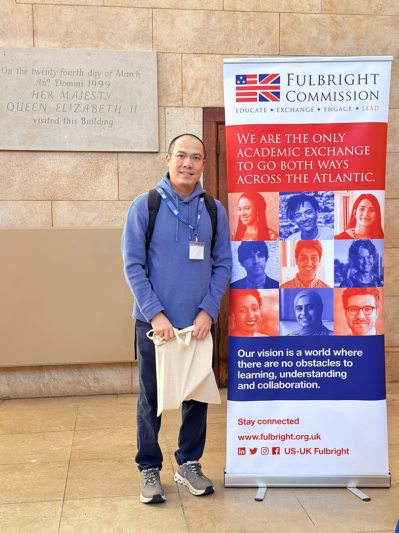 CWU Professor Tanjian Liang stands next to a Fulbright Scholars sign 