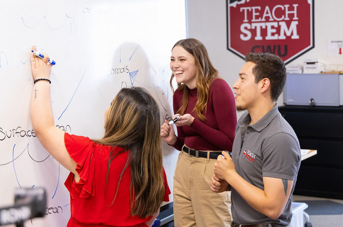 A CWU Teach STEM instructor works with two students in a classroom.