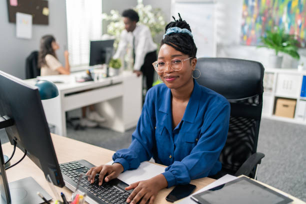 Woman in a blue shirt smiling at her desk.