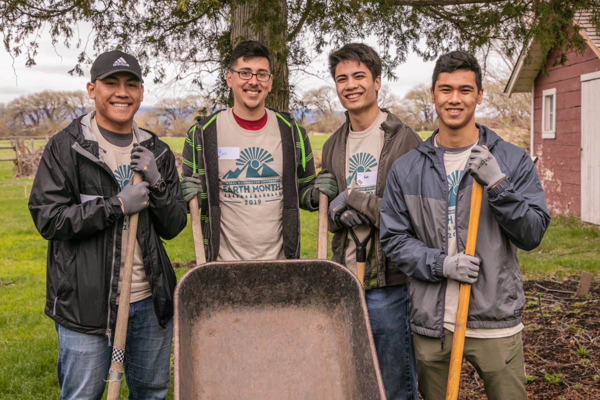4 CWU students posing in front of wheelbarrow and holding shovels