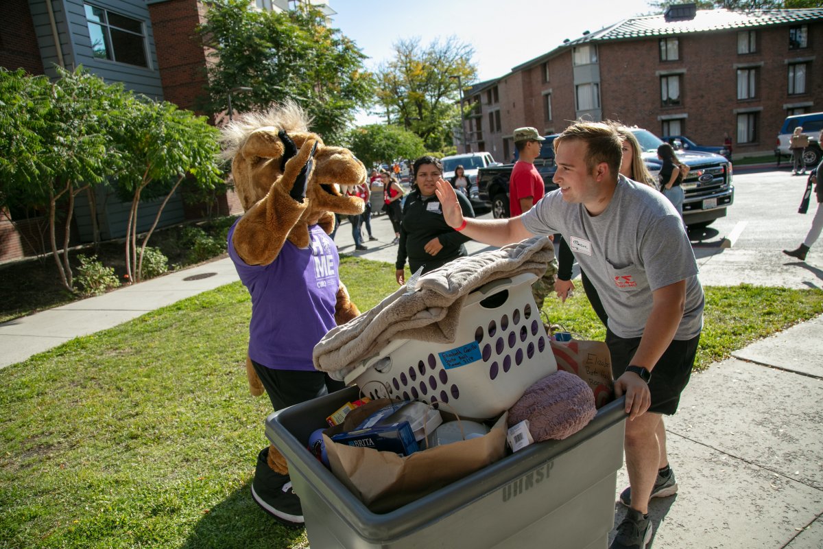 Wellington Wildcat high fives a student behind a laundry cart