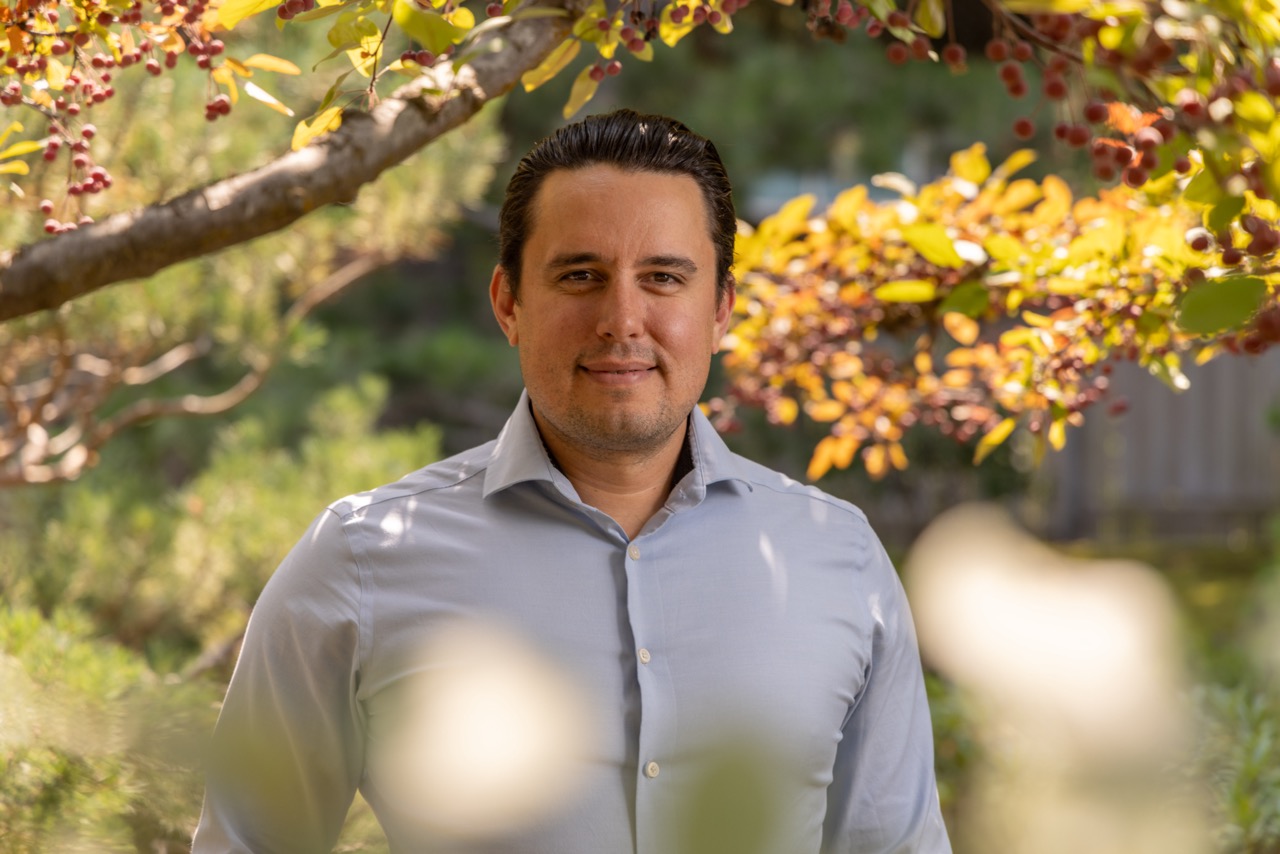 A headshot of Jeff Bousson, he appears to be in front of some trees in by a building on Campus.