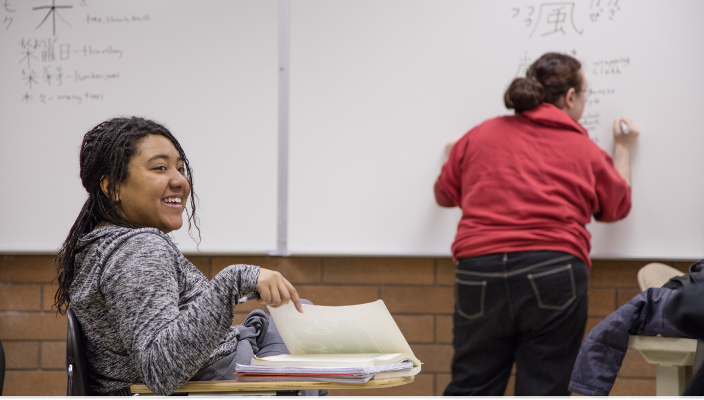 One student writing on the whiteboard and the other is turned around laughing