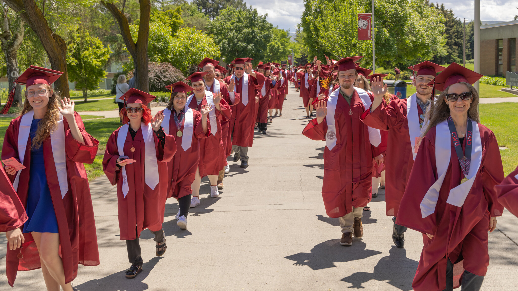 Photo of CWU graduates, smiling and waving as they walk to the commencement ceremony