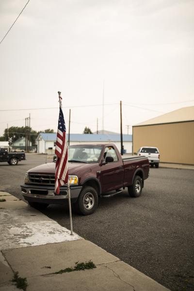 a red Ford pickup truck parked on a street with a flag in front of it. 