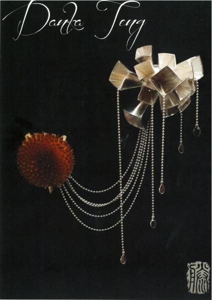 piece of jewelry one part is a red circle and chains connect it to another piece that has metal squares poking out. 