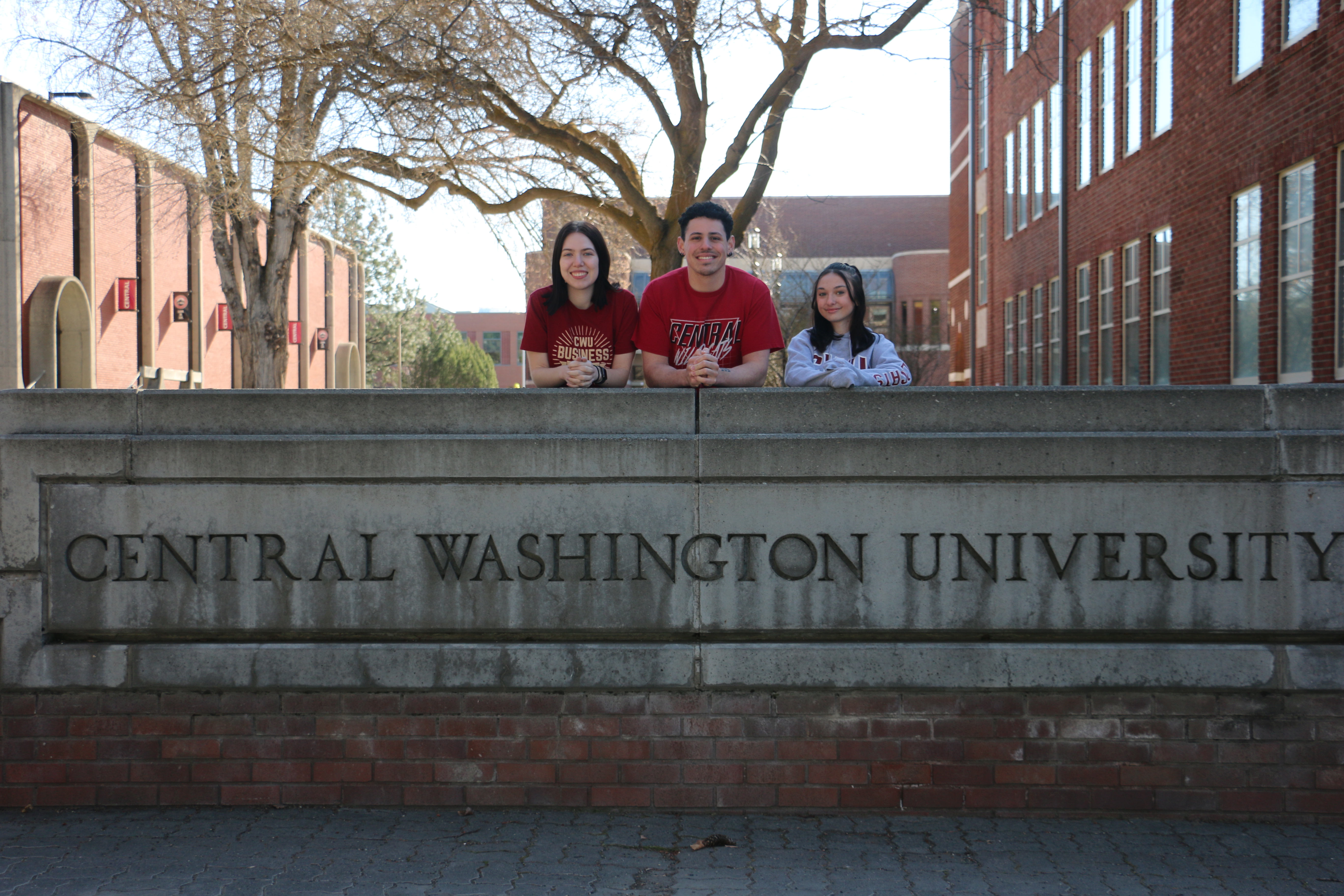 group of 3 students standing behind stone sign that says Central Washington University