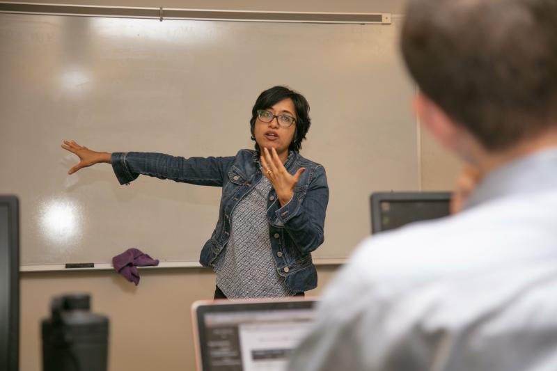 instructor gesturing at whiteboard while addressing class