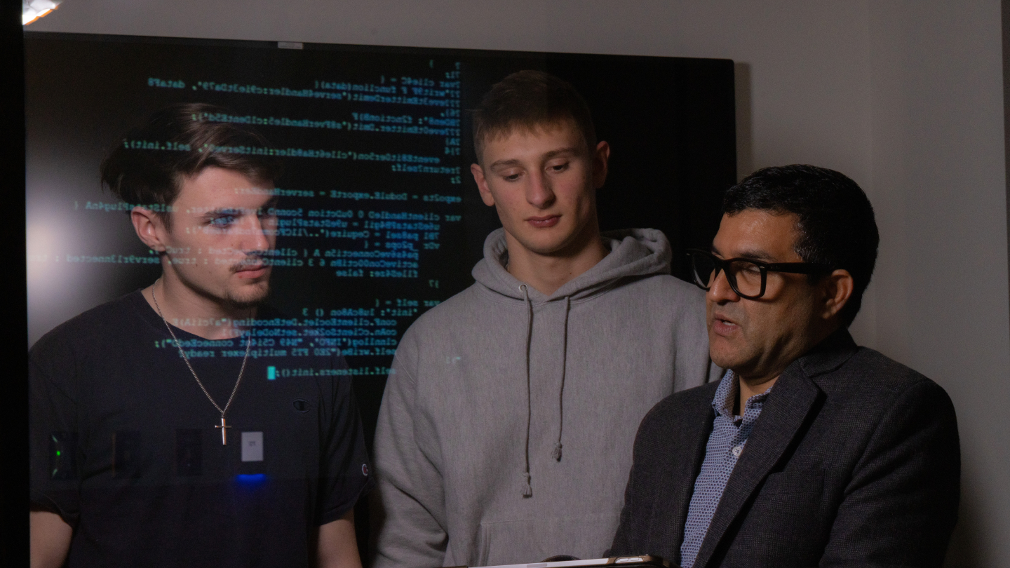 Two students and professor looking at a screen that is reflecting coding over their faces.