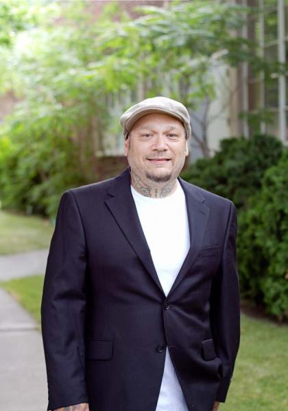Xavier Cavazos smiling in a black suit jacket, white t-shirt, and tan cap