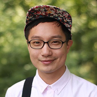 Portrait of Chen Chen wearing a hat and glasses grinning at the camera