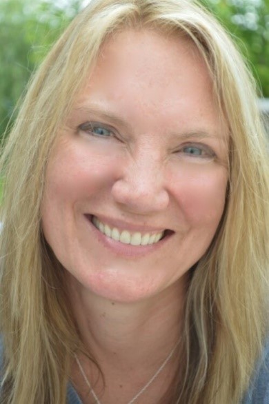 Elise Edie smiling brightly at the camera with green trees behind her