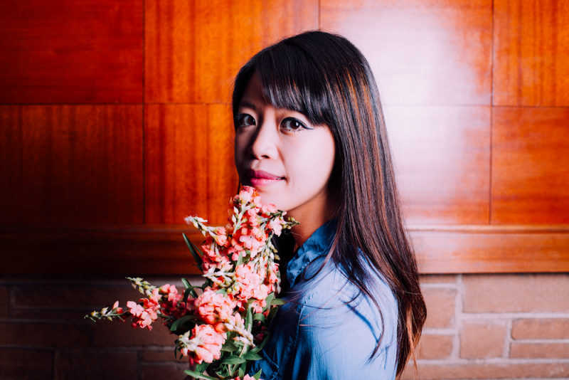 Portrait of Jane Wong wearing a blue blouse and holding a bouquet
