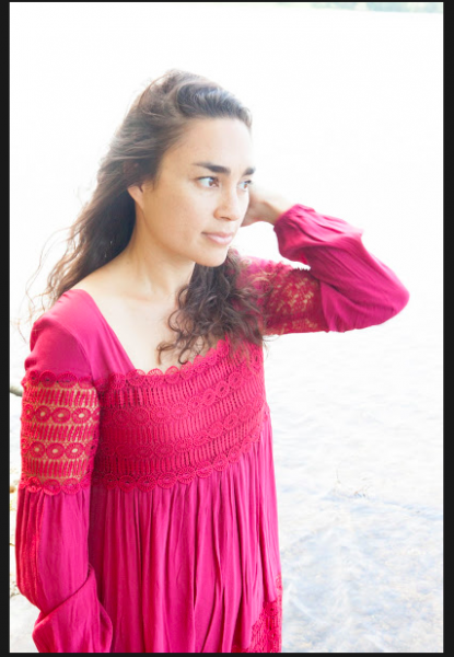 Kristiana Kahakauwila holding her hair in the wind looking off into the water wearing a fuschia dress